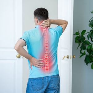 An individual experiencing back pain due to a spinal injury in a bedroom - Diaz-Granados Law Firm